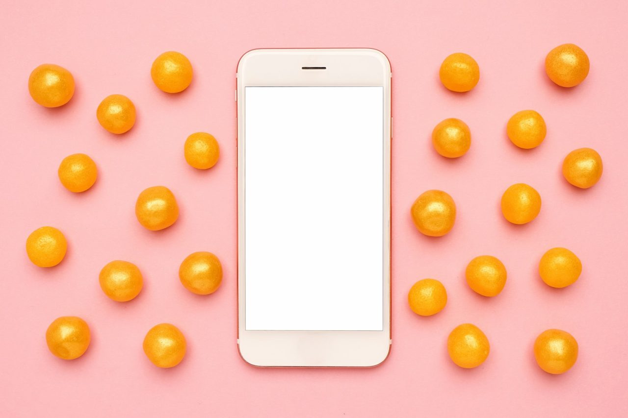 mobile phone and sweet yellow candies on a pink background technology mock up